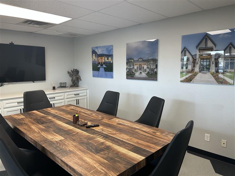 A modern conference room with a wooden table, black chairs, wall art of houses, a TV, and a cabinet with a decorative elephant statue.